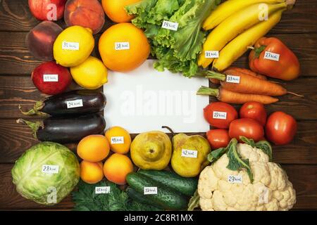 Verschiedene Sorten von rohem Obst und Gemüse mit Kalorienetiketten auf Holztisch und leerem weißem Papier als Kopierplatz für Ihren Text. Ernährung, vegetarische Bio gesunde Ernährung Konzept. Stockfoto