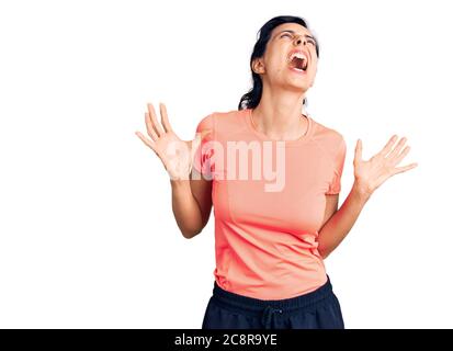 Junge schöne hispanische Frau trägt Sportkleidung verrückt und verrückt schreien und mit aggressivem Ausdruck und Arme angehoben. Frustration Konzept. Stockfoto