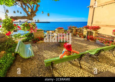 Frau in rot mit Hut in Marciana Marina bei Sonnenuntergang, die blumige Altstadt Borgo al Cotone: Was BAUMWOLLDORF bedeutet. Tourist im Urlaub Reise in Stockfoto