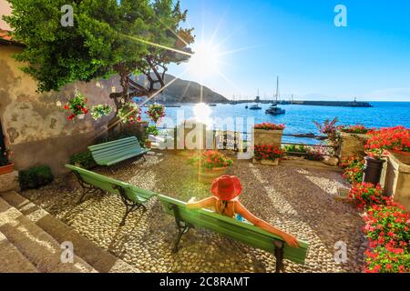 Frau in rot mit Hut in Marciana Marina bei Sonnenuntergang Sonnenstrahlen, die blumige Altstadt Borgo al Cotone: Was bedeutet BAUMWOLLDORF. Tourist im Urlaub Stockfoto