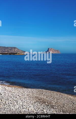 Blick über den tiefblauen Ozean auf den Felsen von Calpe entlang weißem Steinstrand in Albir, Costa Blanca, Spanien Stockfoto