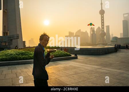 Ein Mann, der am frühen Morgen auf Shanghais Bund am Monument to the People’s Heroes mit der Pudong-Skyline im Hintergrund einen Drachen fliegt. Stockfoto