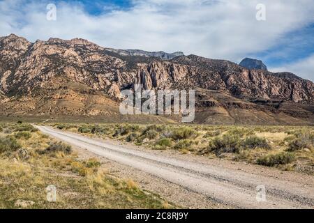 Unbefestigte Straße, die zu Klippen und Felsen aus rosa Granit in Utahs West Desert führt. Der massive Notch Peak ragt über dem Hotel. Stockfoto