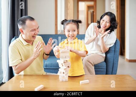 Glückliche vietnamesische Mutter und Vater klatschen zu kleinen Tochter Finishing Turm aus Holzziegeln Stockfoto