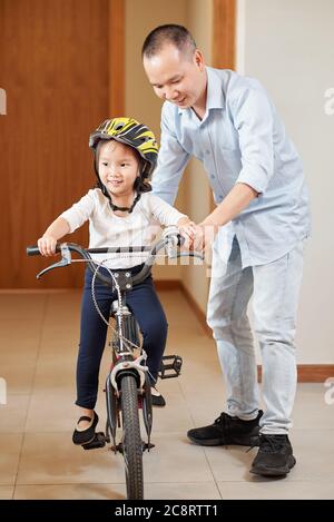 Glücklich vietnamesischen Mann lehrt kleine Tochter, wie man Fahrrad in Wohnung Korridor zu fahren Stockfoto