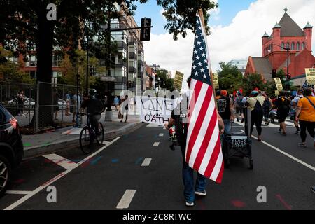 Washington, DC, USA, 25. Juli 2020. Im Bild: Ein Anführer der Veteranen für Black Lives Matter geht die 14. Straße entlang und trägt ein Schild und eine amerikanische Flagge bei einem Marsch gegen Trumps Polizeistaat, der von der Partei für Sozialismus und Befreiung gesponsert wird. Kredit: Allison C Bailey/Alamy Stockfoto