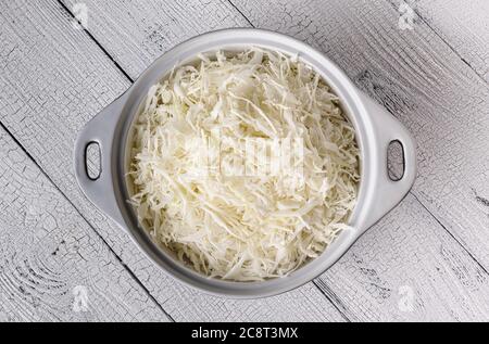 Weiße Keramikschale voll geriebenem Kohl auf alter, weißer Tischfläche aus Brettern. Kochstufe für Krautsalat, fermentierten Kohl und Salat. Fl Stockfoto