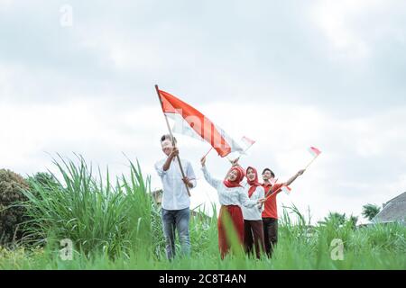 Junge in weiß zu Fuß mit einer indonesischen Flagge mit Stock und drei seiner Freunde gehen hinter ihm mit einer kleinen Flagge Stockfoto