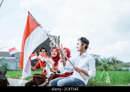 Der junge Mann sitzt mit einem Stock mit indonesischer Flagge und drei seiner Freunde sitzen neben ihm mit vielen kleinen Fahnen auf dem Reisfeld Stockfoto