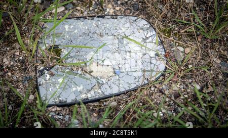 Verprügelte Autospiegel in kleinen Pfauen auf dem Boden nach Unfall. Reflexion des Lichts. Stockfoto