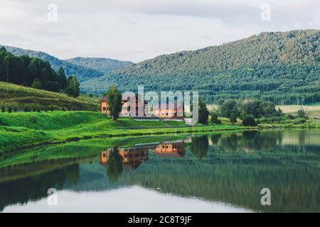 Schöne Landschaft von Bergen und Seen. Das Blockhaus spiegelt sich im klaren Wasser wider. Touristische Basis in den Bergen. Landhaus für Stockfoto