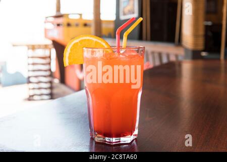 Ein Glas roten Saft auf einem Holztisch. Closeup ocktail von süßen Bourbon Whiskey Drink garniert von Orangenschale auf Tisch Diner Kabine mit verschwommenem Bokeh Stockfoto