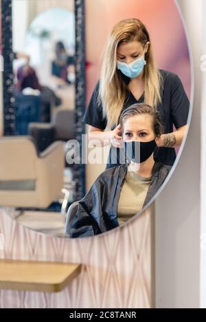 Friseur Trocknen der Haare ihrer Kunden mit einem Haartrockner tragen Schutzmasken in einem Beauty-Center. Stockfoto