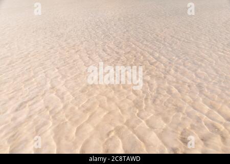 Wellen auf einem gelben sandigen Grund kreuzen sich mit Wellen auf der Wasseroberfläche. Die Textur von Sand und Wasser. Flaches, schwaches, flaches Wasser Stockfoto