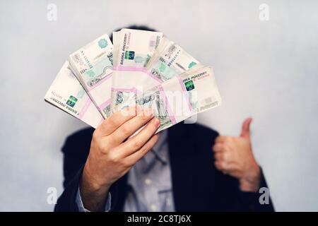 Tausendste Banknoten des russischen Rubel in der Hand eines Mannes. Männliche Hand mit einem Bündel von Banknoten. Überweisung von Geld. Daumen nach oben als Symbol für eine erfolgreiche Stockfoto