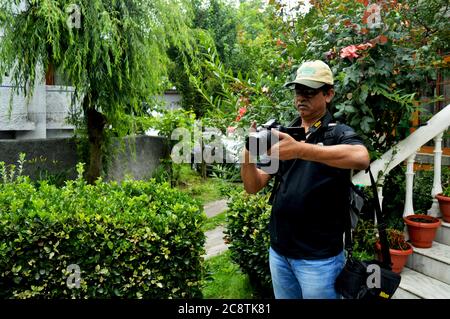 Ein indischer Mann mit Mütze und Brille, der in einem Garten mit Kamera fotografiert und selektiv fokussiert Stockfoto