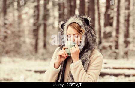 Bester Urlaub. Wärmen Sie sich auf. Frau Winter trinken. Mädchen genießen Glühwein. Frau in Hut trinkt Tee im Wald. Lustige weibliche Pelz-Tiermütze. Wandern und Reisen. Girlhiker trinken Tasse heißen Kaffee. Stockfoto