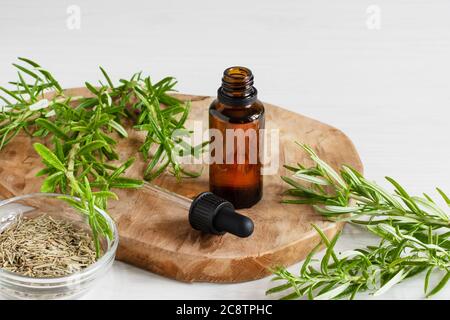 Töls aus Rosmarin ätherischem Öl und frischem Rosmarin Zweig auf weißem Holzgrund. Stockfoto