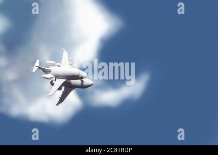 Ein weißes Spielzeugflugzeug steht auf einem Spiegel, der einen blauen Himmel mit Wolken reflektiert. Stockfoto