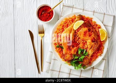 südindische Küche: Tomatenreis aus Basmati, rotes Chilipulver, Zimt, Kardamom, Nelken, serviert mit gebratenen Hühnervierteln, Zitrone auf einem Pl Stockfoto