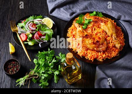 Knusprig gebratene Hühnervierteln mit indischem Tomatenreis und frischem Salat aus Tomaten, Spinat, Gurken, Salat, roter Zwiebel mit Zitronenscheiben Stockfoto