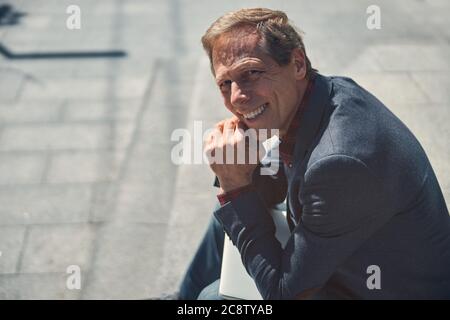 Schöner fröhlicher Mann auf der Straße sitzend Stockfoto
