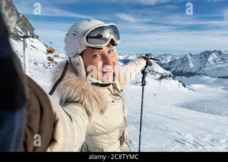 Junge Erwachsene schöne glücklich attraktive kaukasische lächelnde Skifahrer Frau Porträt machen Selfie auf Berggipfel zeigt Skigebiet Panorama Stockfoto