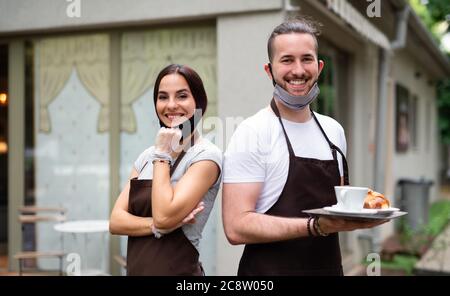 Kellner und Kellnerin mit Gesichtsmaske im Café, Blick auf die Kamera. Stockfoto