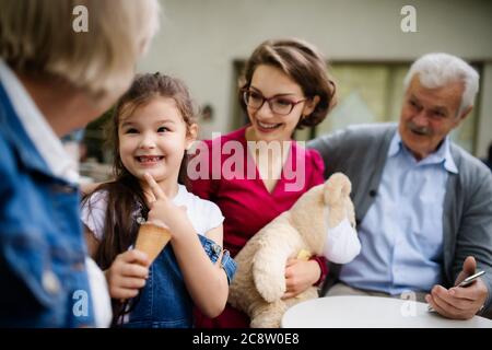 Seniorenpaar mit Tochter und Enkelin sitzen im Café draußen und reden. Stockfoto