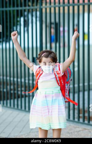 Mädchen trägt eine Maske macht einen Sprung vor Freude auf den Weg zurück zur Schule. Stockfoto