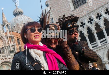 VENEDIG, ITALIEN - 28. FEBRUAR 2020: Zwei Steampunk Masken posieren mit einem Touristen während des Karnevals in Venedig Stockfoto