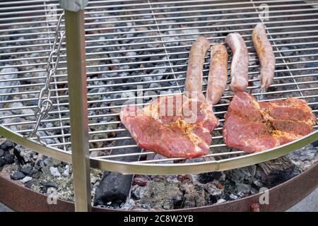 Rohes Fleisch und Bratwurst liegen auf einem Grillrost über dem Ember. Gesehen in Deutschland im Juli. Stockfoto