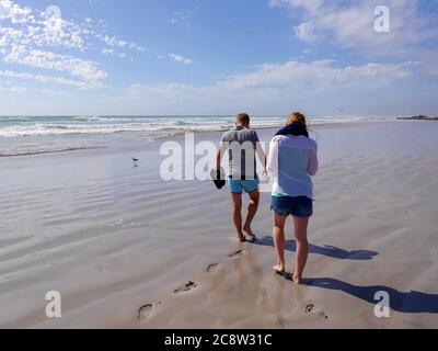 Junges Paar in Sommerkleidung auf menschenleeren, weißen Sandstrand zu Fuß Stockfoto