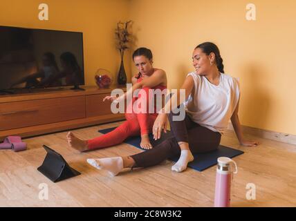 Yoga E-Learning Tablet-Unterricht zu Hause während Coronavirus. Zwei junge Mädchen überprüfen Tablet E-Learning Yoga-Lektionen. Stockfoto