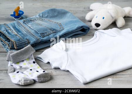 Babykleidung und Accessoires mit weißem Bärenspielzeug auf einem Holzhintergrund Stockfoto