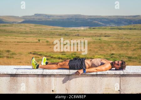 Athletischer gesunder junger Mann, der sich nach einer anstrengenden Wanderung an einem sonnigen Sommertag in den Bergen von Palencia, Spanien, auf einer Steinbank ausruhte. Lifestyle-Konzept Stockfoto