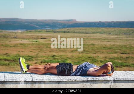 Athletischer gesunder junger Mann, der sich nach einer anstrengenden Wanderung an einem sonnigen Sommertag in den Bergen von Palencia, Spanien, auf einer Steinbank ausruhte. Lifestyle-Konzept Stockfoto