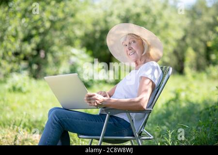 Ältere Frau, die mit dem Computer im Liegestuhl sitzt Stockfoto