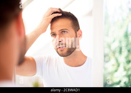 Nahaufnahme eines hübschen jungen T-Shirts, während er sein Gesicht im Badezimmerspiegel bewundert. Stockfoto