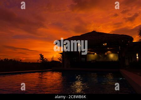 Schöner orange feuriger Sonnenuntergang in den Tropen. Straßendach von Heu, neben dem Pool und mit Blick auf das Reisfeld Stockfoto