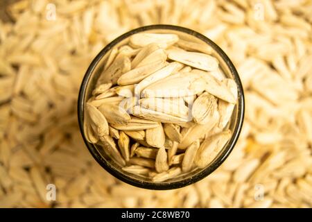 Weiße Sonnenblumenkerne, die mit Meersalz in einem Glas gebraten werden, und Sonnenblumenkerne, die auf einem Hintergrund aus grobstrukturiertem Grappenkerz verstreut sind. Nahaufnahme Stockfoto