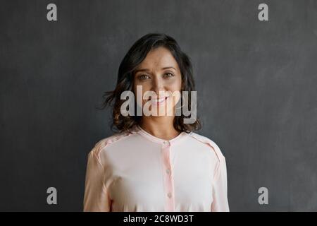 Porträt einer jungen asiatischen Geschäftsfrau, die lächelt, während sie allein vor einer leeren Kreidetafel steht Stockfoto