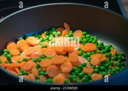 Schnell garen Erbsen mit Karottenscheiben in der Pfanne Stockfoto