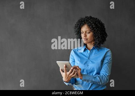 Geschäftsfrau, die mit einem digitalen Tablet arbeitet, während sie vor einer leeren Kreidetafel im Büro steht Stockfoto