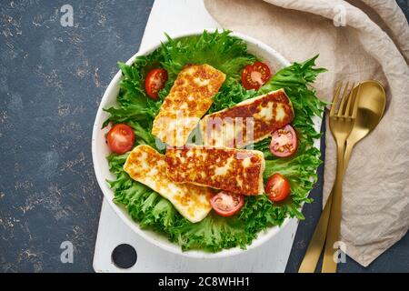 Veganer Salat mit gebratenen Halloumi und Tomaten, dunkler Hintergrund, Draufsicht Stockfoto