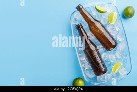 Sommer mit Getränk. Zwei Glasflaschen in Glastablett mit Eis und Limette auf blauem Hintergrund Stockfoto