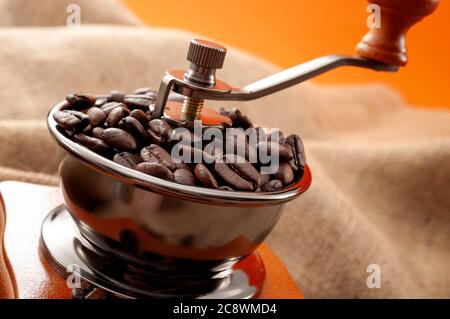 Altmodische Morgen Rituale und Geschmack Erhaltung Mahlprozess Konzept mit Kaffeebohnen in vintage manuelle Mühle auf orange rustikalen Hintergrund Stockfoto