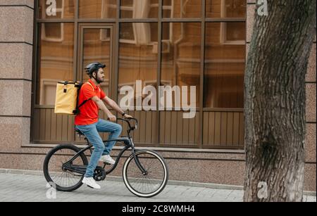 Schnelle Lieferung in der Stadt. Junger Mann mit Helm und Lieferung Rucksack fährt Fahrrad Stockfoto