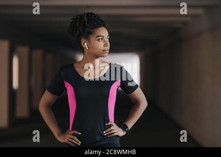 Serious afroamerikanische Mädchen in Sportbekleidung mit kabellosen Kopfhörern und Fitness-Tracker Stockfoto