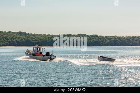 Kleines Fischerboot, das einen kleinen Dingy vor der Küste von Shelter Island, NY zieht Stockfoto